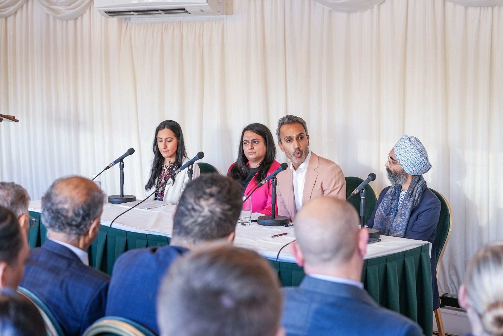 Priyaneet Kainth speaking on the Asian Voice panel alongside three fellow panellists at microphones, with an audience in the foreground.