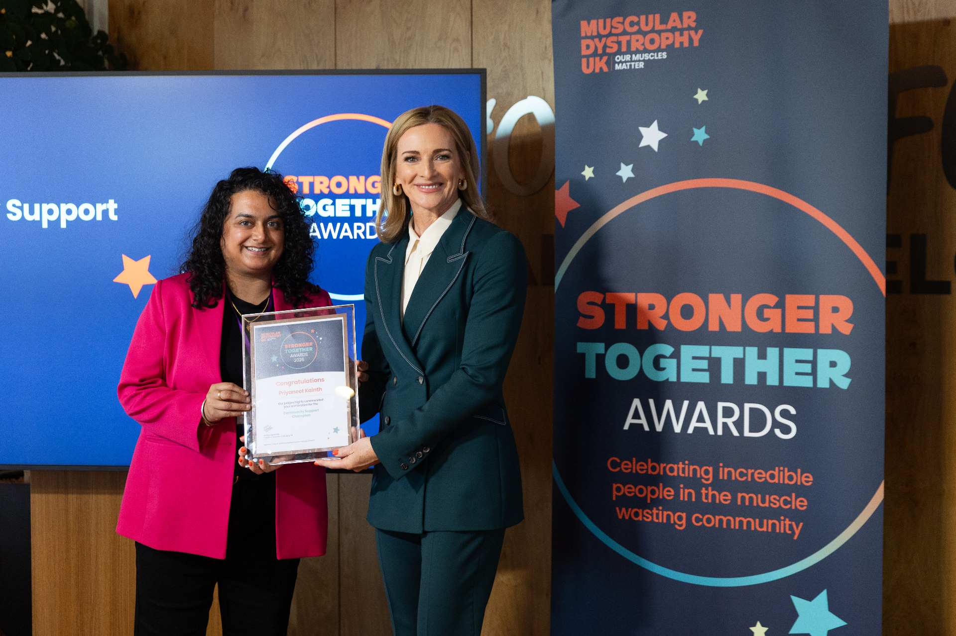 Priyaneet Kainth, wearing a pink blazer, holding a Stronger Together Awards 2026 certificate alongside television presenter Gabby Logan, with a Muscular Dystrophy UK banner in the background.