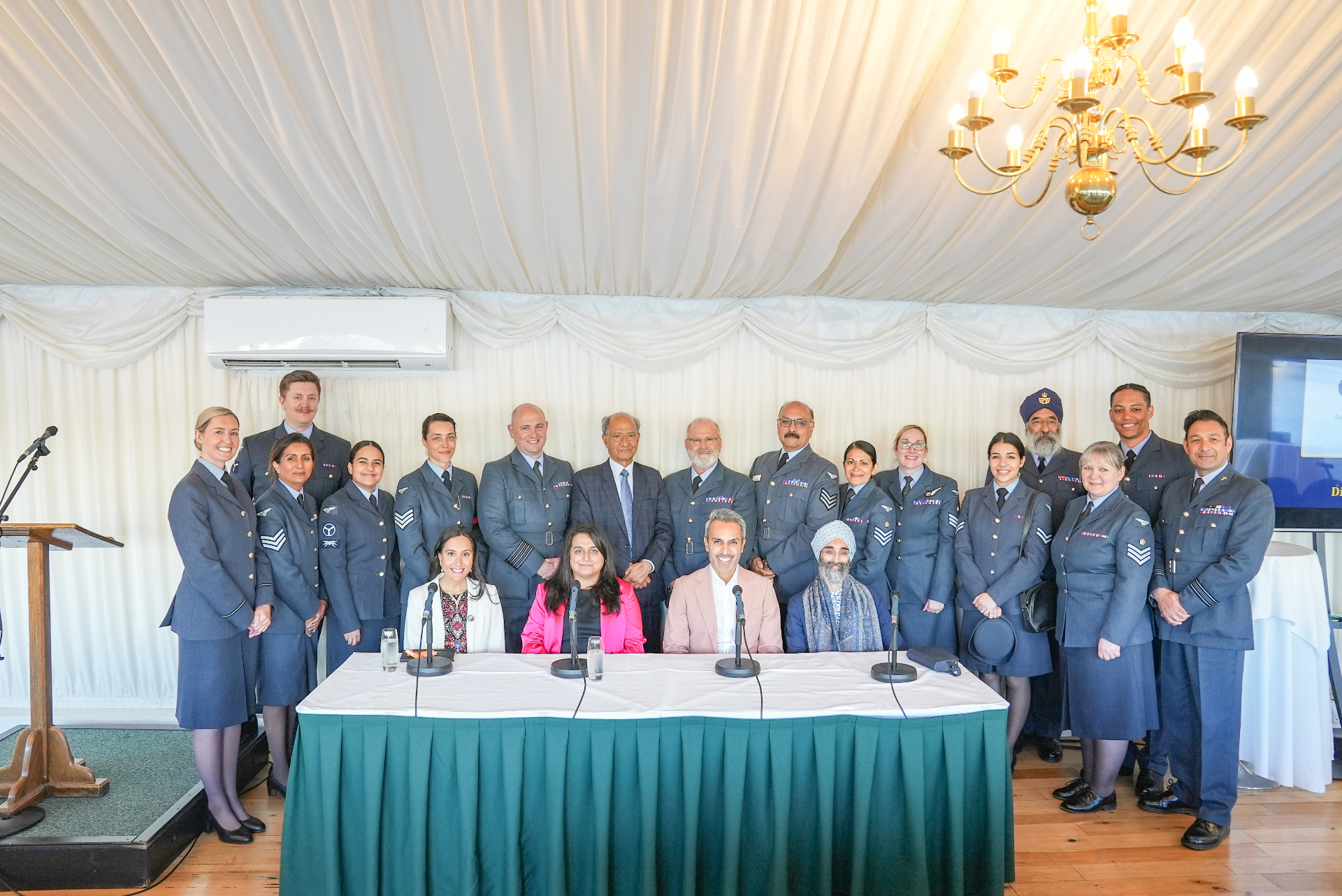 Group photo of the Asian Voice Be the Change panellists with Royal Air Force personnel at the House of Commons, with Priyaneet Kainth seated at the front table in a pink blazer.